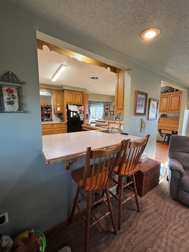 kitchen with brown cabinets, a kitchen breakfast bar, freestanding refrigerator, a textured ceiling, and a sink