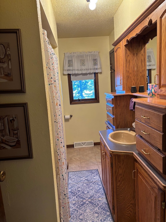 bathroom with visible vents, vanity, a textured ceiling, baseboards, and tile patterned floors