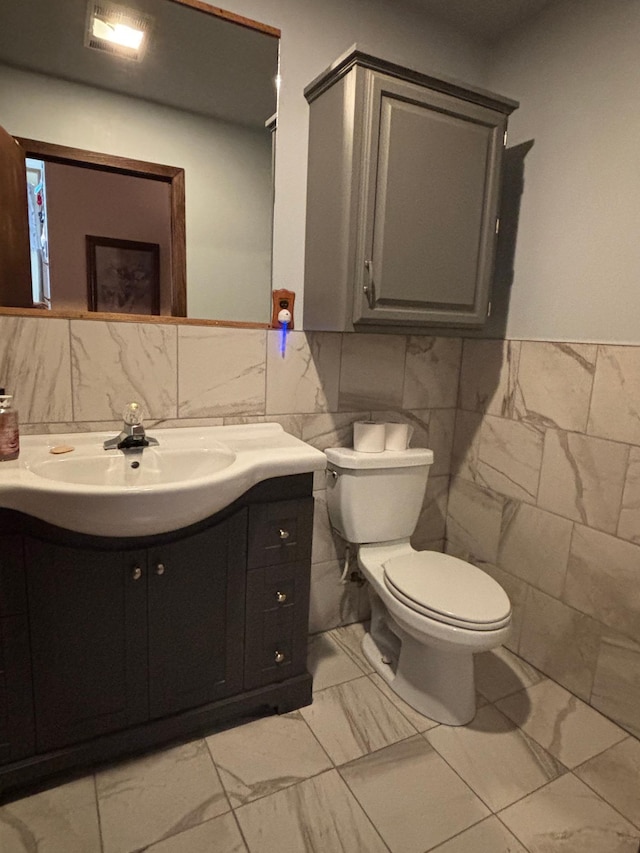 half bathroom with tile walls, marble finish floor, vanity, and toilet