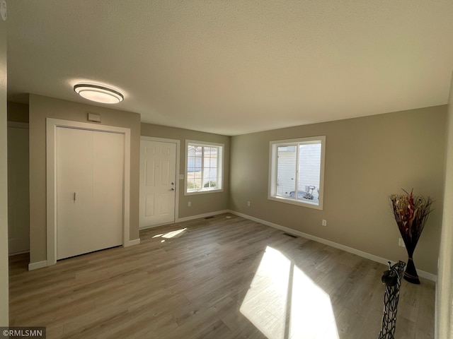 foyer featuring visible vents, a textured ceiling, baseboards, and wood finished floors