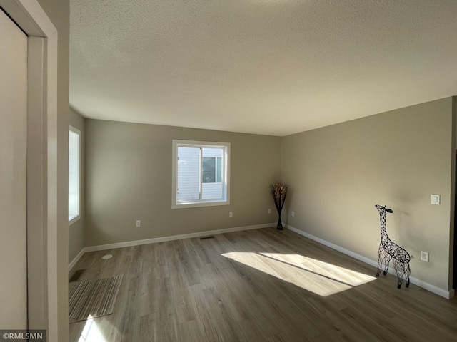 spare room with visible vents, a textured ceiling, baseboards, and wood finished floors