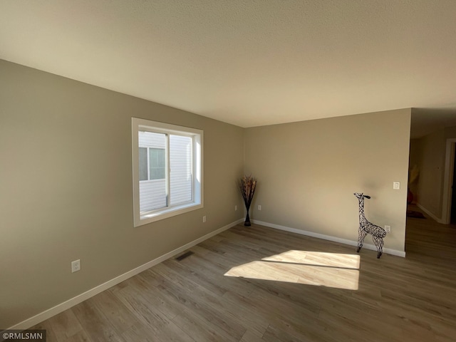 spare room featuring baseboards, visible vents, and wood finished floors