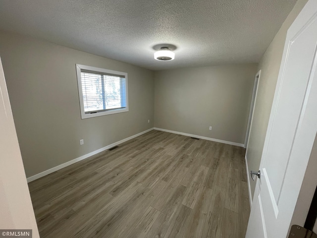 unfurnished bedroom with a textured ceiling, wood finished floors, visible vents, and baseboards