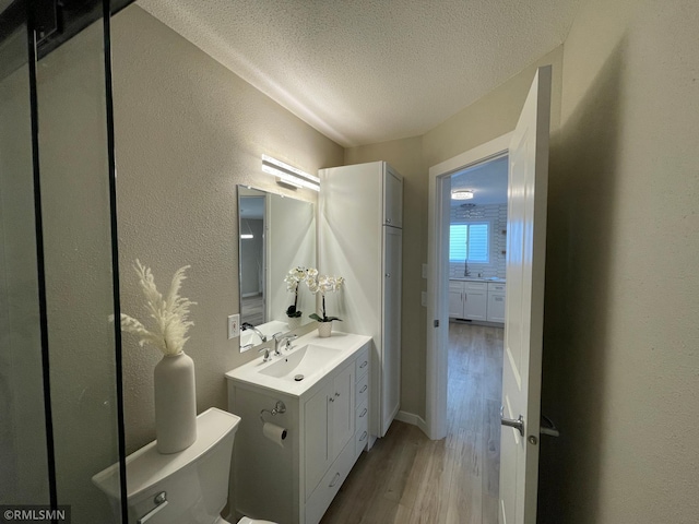 bathroom featuring a textured wall, toilet, wood finished floors, a textured ceiling, and vanity