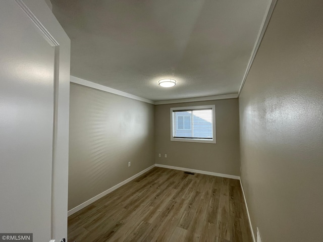 empty room featuring crown molding, a textured ceiling, baseboards, and wood finished floors