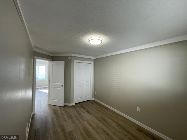 empty room with crown molding, a textured ceiling, baseboards, and wood finished floors