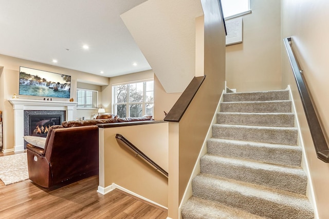 stairway featuring a high end fireplace, baseboards, recessed lighting, and wood finished floors