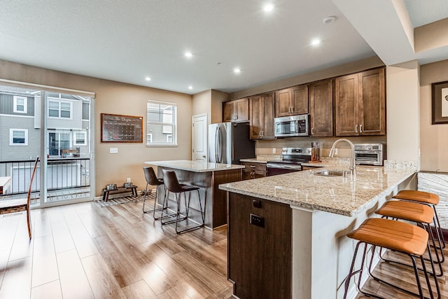 kitchen with light wood finished floors, stainless steel appliances, a sink, a kitchen island, and a kitchen bar