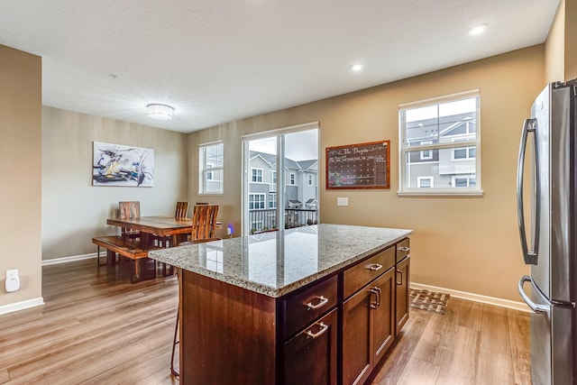 kitchen featuring light wood-style floors, freestanding refrigerator, light stone counters, and baseboards