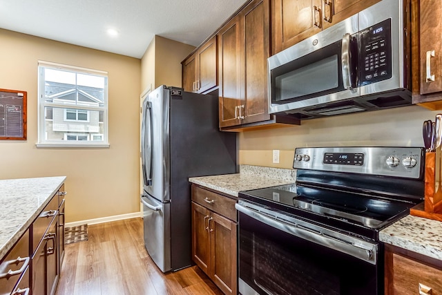 kitchen featuring light stone countertops, light wood-style floors, baseboards, and stainless steel appliances