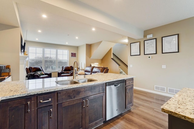 kitchen featuring light wood-style flooring, open floor plan, dark brown cabinets, stainless steel dishwasher, and a sink