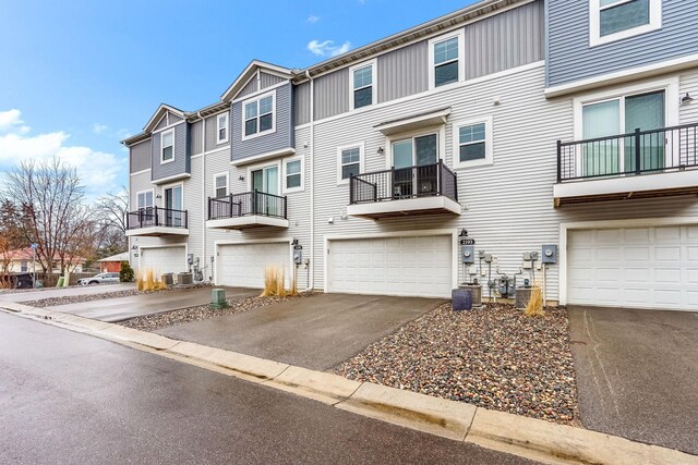 view of property with driveway, an attached garage, a residential view, and central AC unit