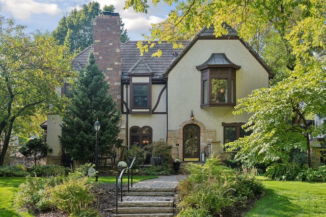 tudor home with a chimney, a front yard, and stucco siding