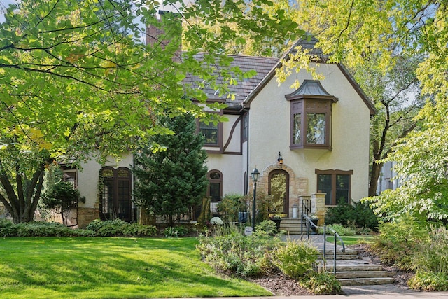 tudor home with stone siding, a front lawn, and stucco siding