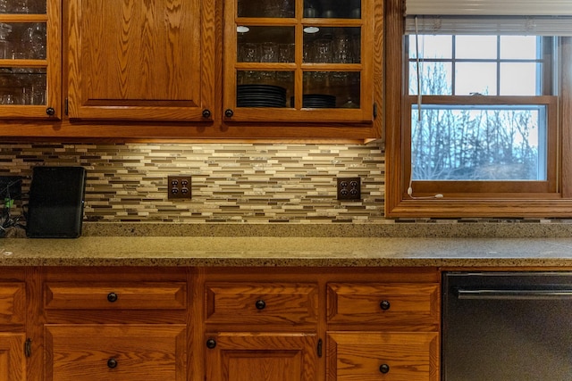 kitchen with tasteful backsplash, glass insert cabinets, brown cabinetry, and light stone counters