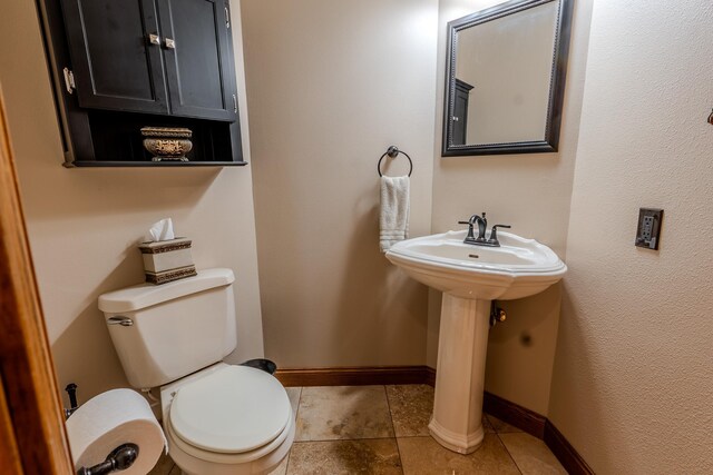 half bathroom with a sink, toilet, baseboards, and tile patterned floors