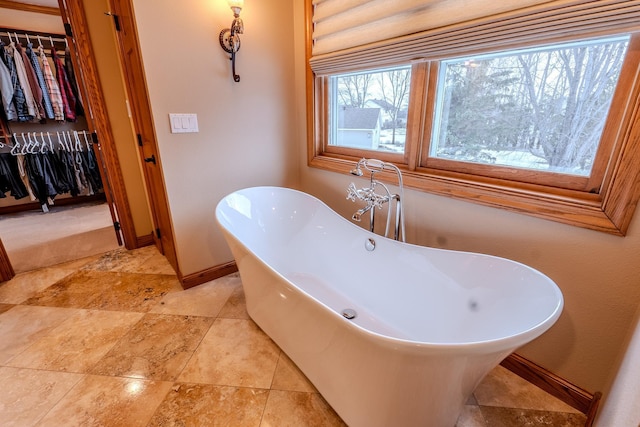 bathroom with a freestanding bath, a spacious closet, and baseboards