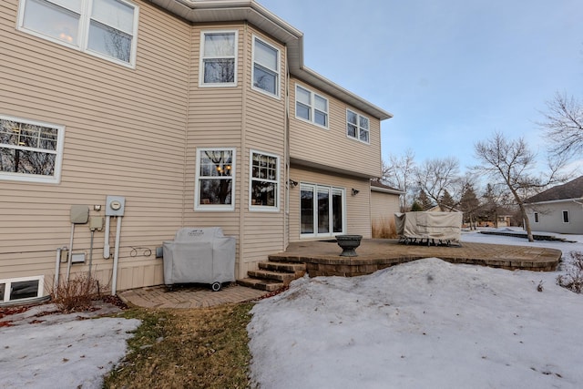 snow covered back of property with a patio