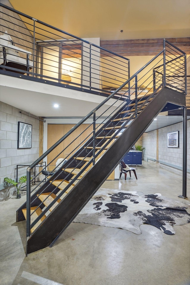 staircase featuring concrete block wall, a towering ceiling, and concrete flooring