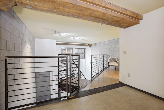 corridor with concrete block wall, concrete floors, an upstairs landing, baseboards, and rail lighting