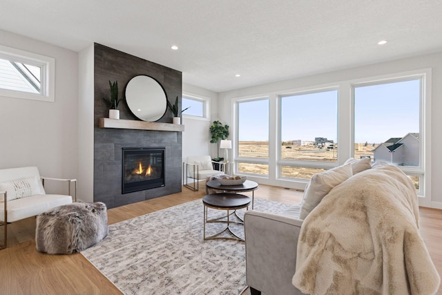 living area with a tiled fireplace, plenty of natural light, wood finished floors, and recessed lighting