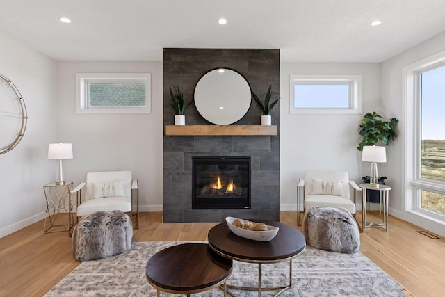 living area featuring baseboards, wood finished floors, a wealth of natural light, and a tile fireplace