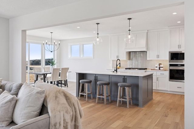 kitchen with custom exhaust hood, appliances with stainless steel finishes, open floor plan, white cabinets, and a sink