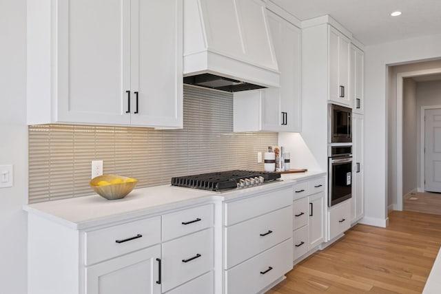 kitchen with white cabinetry, premium range hood, appliances with stainless steel finishes, and backsplash