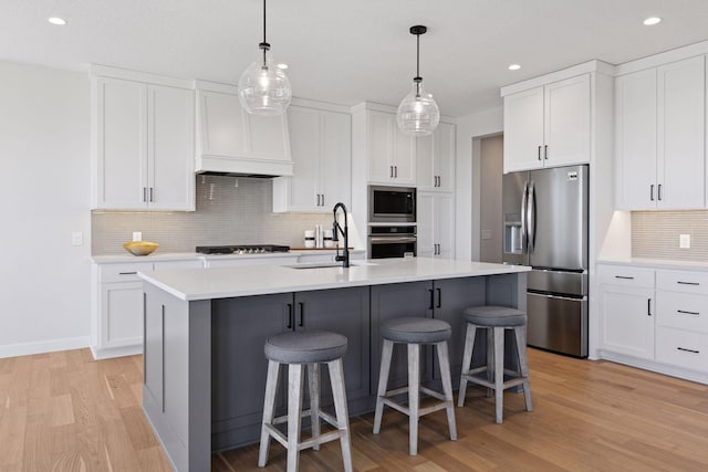 kitchen with stainless steel appliances, a sink, light wood-style floors, a kitchen breakfast bar, and light countertops