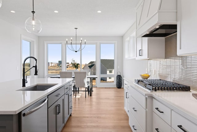 kitchen with light wood finished floors, custom exhaust hood, stainless steel appliances, backsplash, and a sink