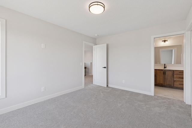 unfurnished bedroom with light carpet, ensuite bath, a sink, and baseboards