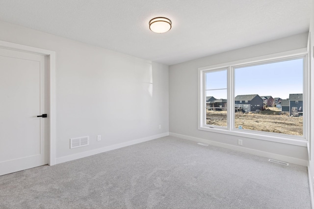 carpeted spare room featuring baseboards, visible vents, and a textured ceiling