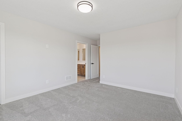 spare room featuring a textured ceiling, light colored carpet, visible vents, and baseboards