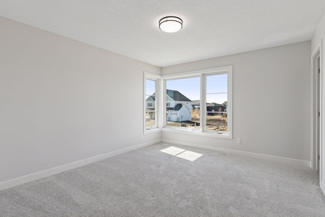 carpeted spare room featuring a textured ceiling and baseboards