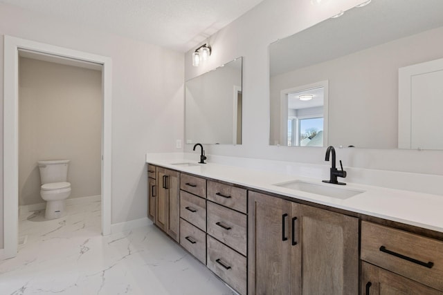 full bath featuring marble finish floor, double vanity, a sink, and baseboards