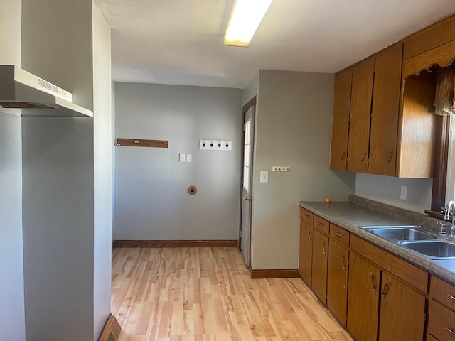 kitchen featuring brown cabinetry, a sink, light wood-style flooring, and baseboards