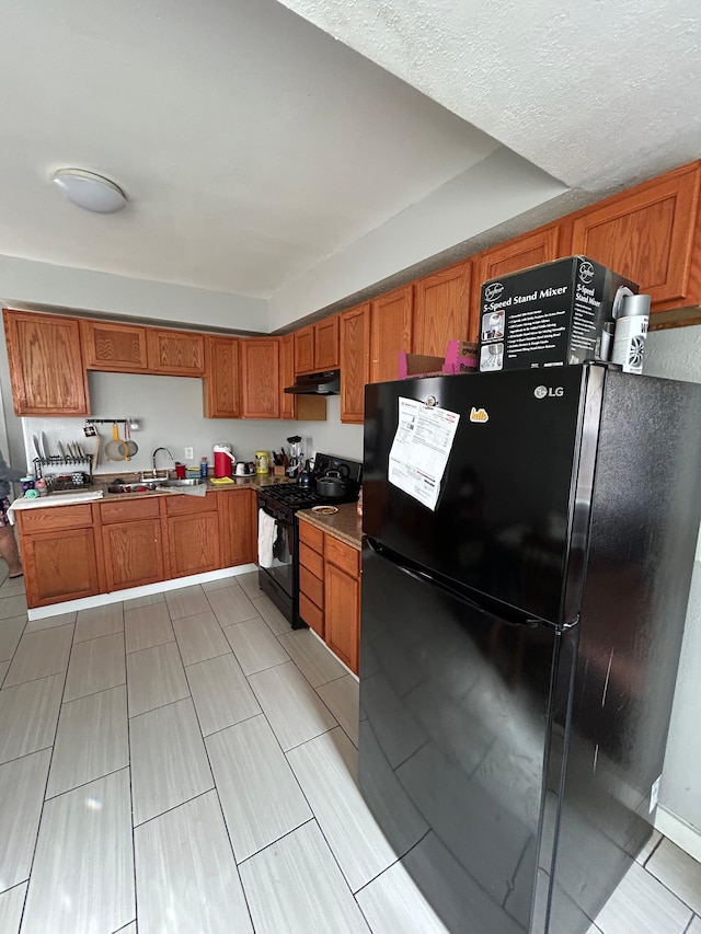 kitchen featuring black appliances, brown cabinetry, a sink, and under cabinet range hood