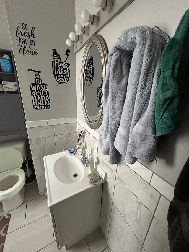 bathroom featuring toilet, a wainscoted wall, tile walls, and vanity