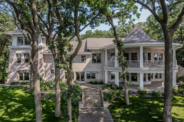 view of front of house with a front yard, a patio area, brick siding, and a balcony