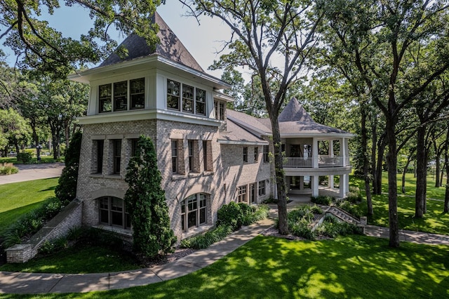 view of front of property featuring brick siding, a balcony, and a front lawn