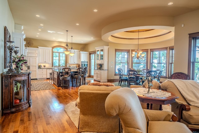 living area featuring an inviting chandelier, a raised ceiling, a wealth of natural light, and light wood-style floors