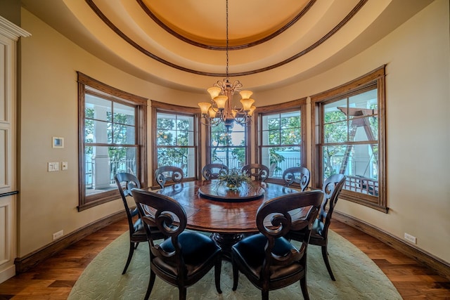 dining room featuring dark wood-type flooring, a tray ceiling, a chandelier, and a healthy amount of sunlight