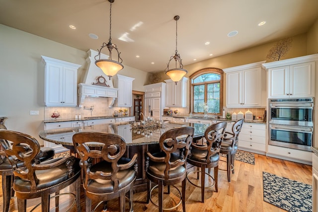 kitchen with a large island, custom range hood, a breakfast bar area, stainless steel appliances, and light wood-type flooring