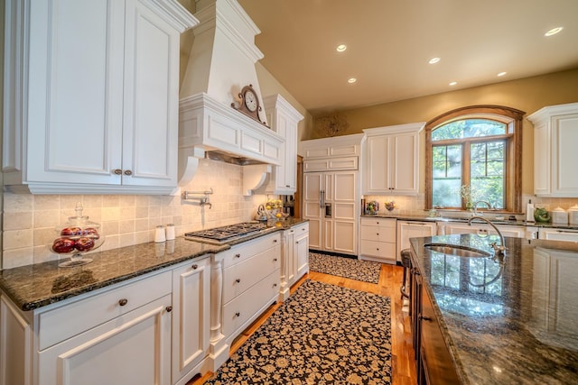 kitchen featuring decorative backsplash, custom range hood, stainless steel appliances, light wood-style floors, and white cabinetry
