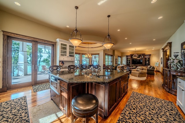 kitchen featuring a center island with sink, light wood-style flooring, dark brown cabinetry, a sink, and dark stone countertops