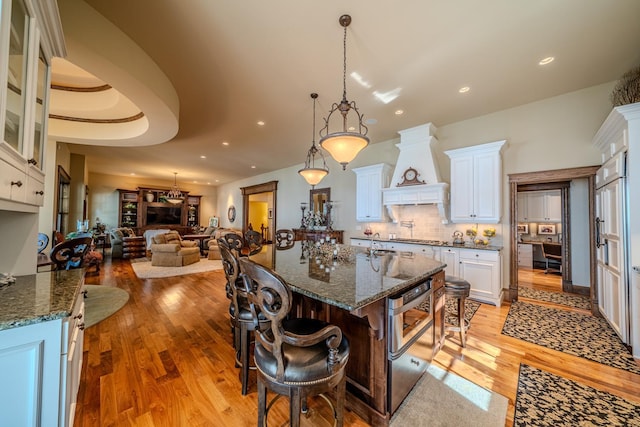 kitchen featuring custom range hood, light wood-style floors, open floor plan, white cabinetry, and a kitchen breakfast bar