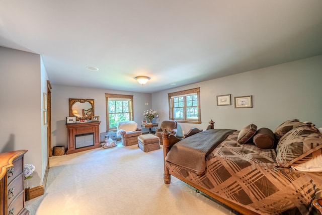 bedroom with a glass covered fireplace and light colored carpet