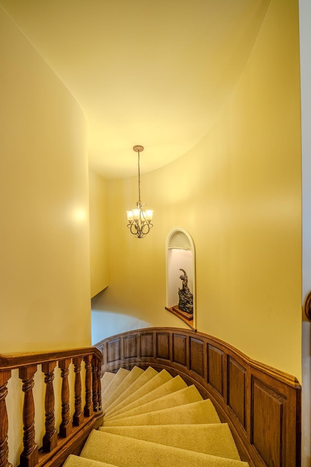 staircase featuring a wainscoted wall and a notable chandelier