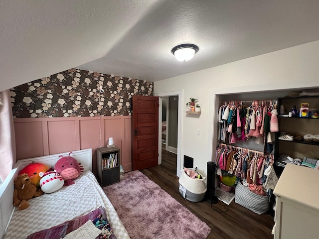 bedroom with wood finished floors, wallpapered walls, wainscoting, a closet, and a textured ceiling