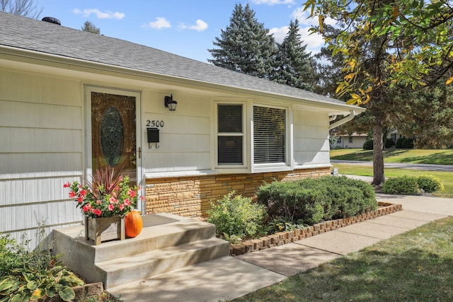 view of exterior entry featuring stone siding and roof with shingles